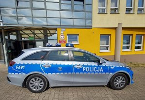 radiowóz policyjny na tle Komendy Powiatowej Policji w Wieruszowie a na nim czapki policyjne funkcjonariuszy ruchu drogowego.