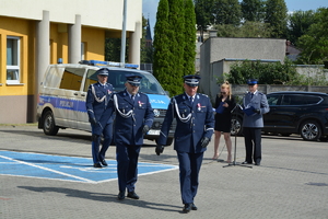 widzimy I Zastępcę Komendanta Wojewódzkiego Policji w Łodzi inspektora Jarosławowa Rybkę, dowódcę uroczystości oraz idącego za nimi Komendanta Powiatowego Policji w Wieruszowie inspektora Grzegorza Dzierzkowskiego, w tle radiowóz i budynek komendy.