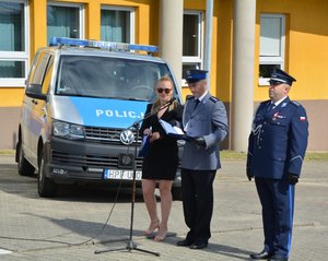 widzimy lektora prowadzącego oraz kadrowego, a także dowódcę uroczystości na tle Komendy Powiatowej Policji w Wieruszowie i radiowozu policyjnego.