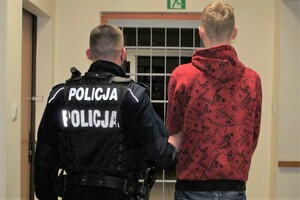 korytarz komendy, umundurowany policjant prowadzi zatrzymanego mężczyznę.