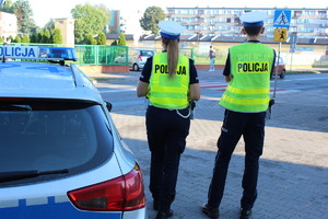 policjanci podczas nadzoru nad ruchem drogowym na tle radiowozu.