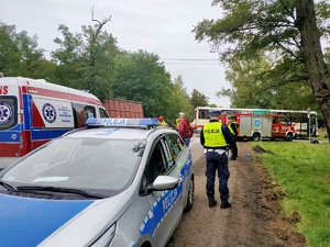 Na zdjęciu radiowóz policyjny, karetka pogotowia straż pożarna oraz policjant ruchu drogowego wykonujący czynności. W tle autobus.