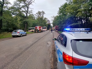 Na zdjęciu widoczny radiowóz policyjny oraz całe miejsce zdarzenia. W tle pojazd straży pożarnej, strażacy oraz autobus i pojazd ciężarowy.