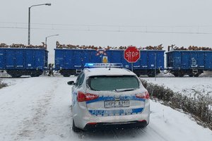 radiowóz na przejeździe kolejowym w tle skład pociągu Cargo.