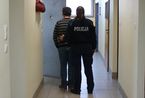 zatrzymany w policyjnym areszcie w asyście policjanta.