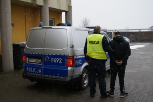 policjant z zatrzymanym w tle radiowóz.