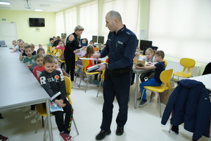 policjant wręcza element odblaskowy uczestnikom spotkania.