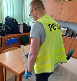 Policjant podczas oględzin przedmiotu drewnianego którym posługiwał się sprawca.