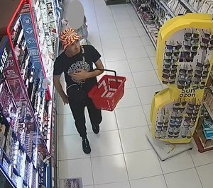 mężczyzna chodzi po sklepie, na głowie ma założoną pomarańczową wzorzystą czapkę – kapelusz, granatową koszulkę z krótkim rękawem i w ręku trzyma koszyk na zakupy.