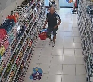 mężczyzna trzymający koszyk na zakupy w ręku, ubrany jest w szare spodenki i granatowo białą koszulkę polo. Na prawej nodze ma założoną opaskę.