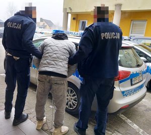 policjanci prowadzą zatrzymanego mężczyznę do radiowozu.