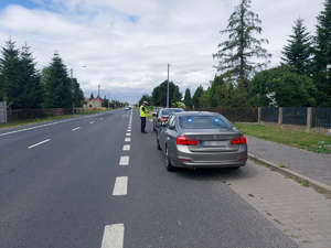 widzimy policjanta stojącego przy samochodzie osobowym, widzimy również nieoznakowany radiowóz marki BMW.