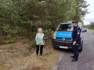 widzimy policjanta i osobę z koszykiem grzybów stojących przy radiowozie w tle widać las.