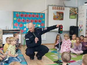 widzimy policjanta pokazującego sygnalizator świetlny dzieciom.