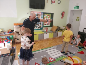 policjant prowadzi zajęcia w klasie widzimy dziewczynkę i chłopca.