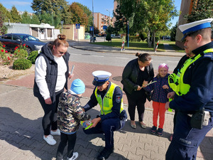 widzimy policjantów i dzieci wraz z opiekunami otrzymujące odblaski od funkcjonariuszy.