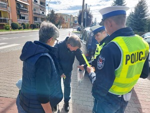 widzimy policjantów i dzieci wraz z opiekunami otrzymujące odblaski od funkcjonariuszy.