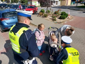 widzimy policjantów i dzieci wraz z opiekunem otrzymujące odblaski od funkcjonariuszy.