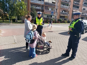 widzimy policjantów i dzieci wraz z opiekunem otrzymujące odblaski od funkcjonariuszy.