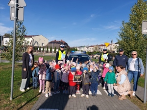 grupowe zdjęcie z dziećmi ich opiekunami i policjantami na tle radiowozu na miasteczku ruchu drogowego.