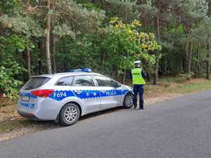 policjant stojący przy radiowozie w tle widać las.