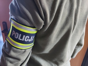 widzimy policjanta nieumundurowanego z założoną opaska policyjną.