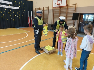 policjanci wręczają kamizelki odblaskowe dzieciom.