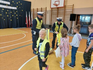 policjanci wręczają kamizelki odblaskowe dzieciom.