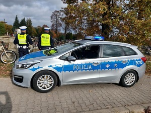 policjanci stoją przy radiowozie w tle widać cmentarz.