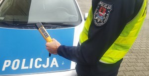 policjant przy radiowozie i trzyma w ręku urządzenia do badania stanu trzeźwości.