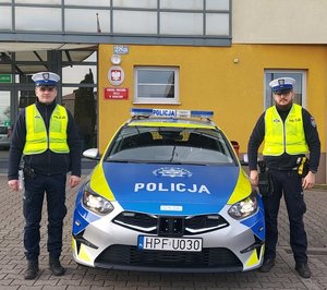 widzimy policjantów stojących przy radiowozie na tle Wieruszowskiej komendy.