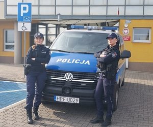 widzimy policjantki stojące na tle komendy przy radiowozie.