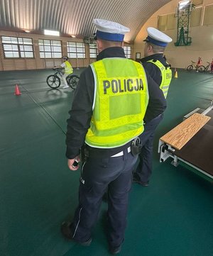 widzimy  policjantów na torze przeszkód egzaminu karty rowerowej oraz jego uczestnika jadącego rowerem.