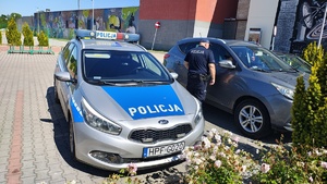 widzimy policjanta obok radiowozu policyjnego, zaglądającego do stojącego obok samochodu osobowego.
