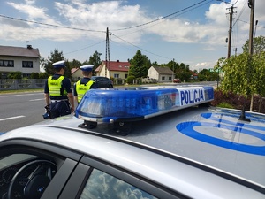 widzimy policjantów stojących przy drodze na tle radiowozu.