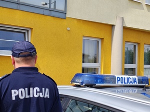 widzimy policjanta stojącego przy policyjnym radiowozie na tle Komendy Powiatowej Policji w Wieruszowie.