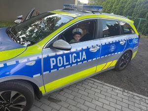 widzimy chłopca siedzącego w radiowozie policyjnym z założona czapką policjanta.