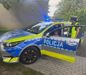 widzimy dziecko w radiowozie a obok stojąca policjantkę.