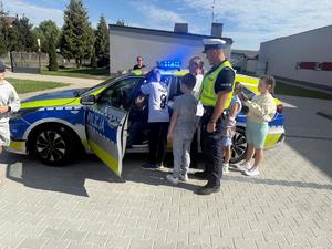 dzieci i policjant w tle radiowóz