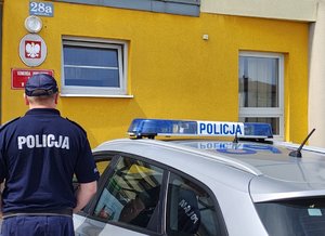 widzimy policjanta stojącego przy radiowozie na tle budynku wieruszowskiej komendy.