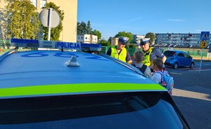 widzimy policjantów rozmawiających z dziećmi na tle radiowozu.