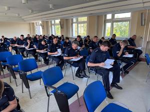 widzimy policjantów piszących test wiedzy w sali wykładowej.