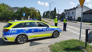 widzimy policjantów mierzących prędkość kierowcom w tle poruszający się pojazd i radiowóz policyjny.
