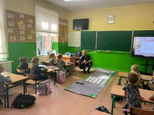 widzimy policjanta prowadzącego zajęcia na macie edukacyjnej.