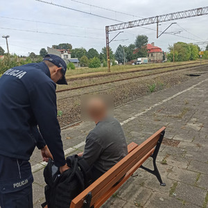 widzimy policjanta kontrolującego mężczyznę siedzącego na ławce.