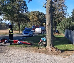 widzimy miejsce wypadku drogowego na którym widać strażaka stojącego na jezdni, radiowóz policyjny, rower oraz samochód osobowy.