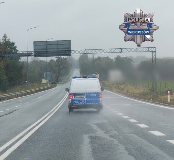 widzimy radiowóz policyjny jadący po drodze, a w prawym górnym roku widzimy odznakę policyjną z napisem Policja Wieruszów.