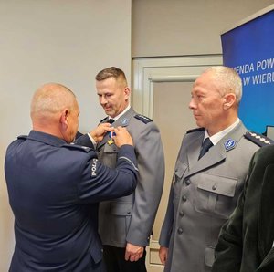widzimy odznaczonego policjanta oraz wręczających odznaczenia.