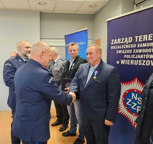 widzimy odznaczonego policjanta oraz wręczających odznaczenia.