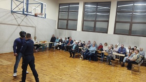 widzimy policjantów pokazujących chwyty obezwładniające oraz uczestników spotkania.